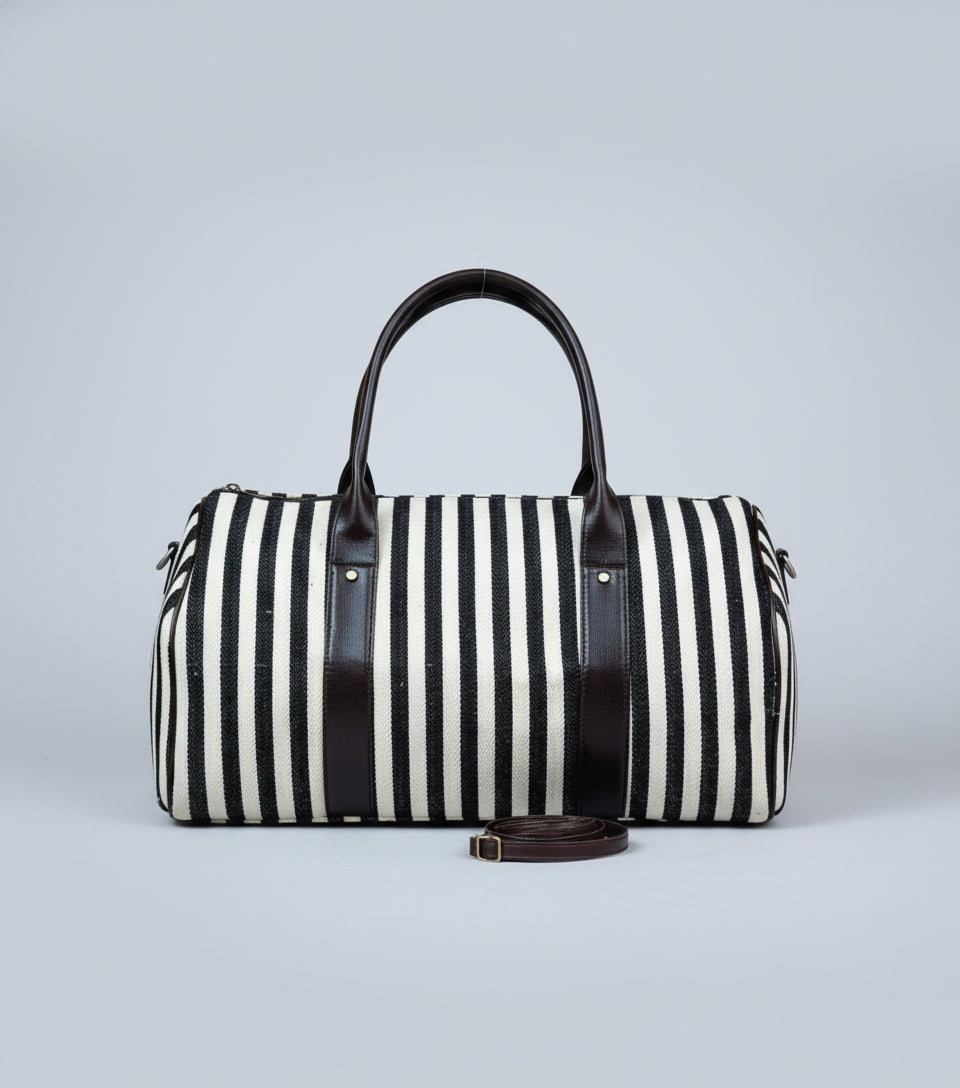 Black and white striped duffel bag with brown leather straps on a textured surface.