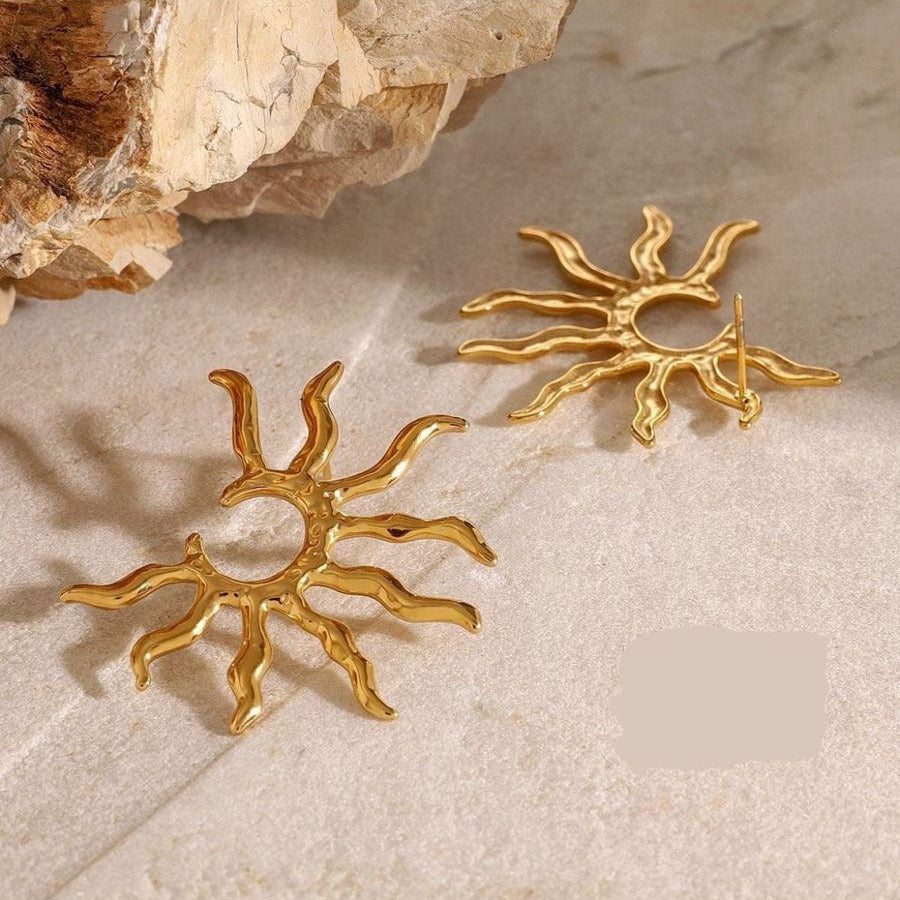 Gold sun-shaped earrings on a textured beige surface