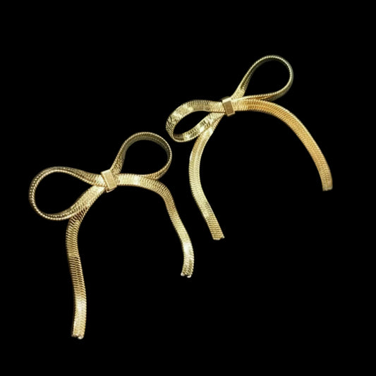 Gold bow-shaped earrings on a black glove