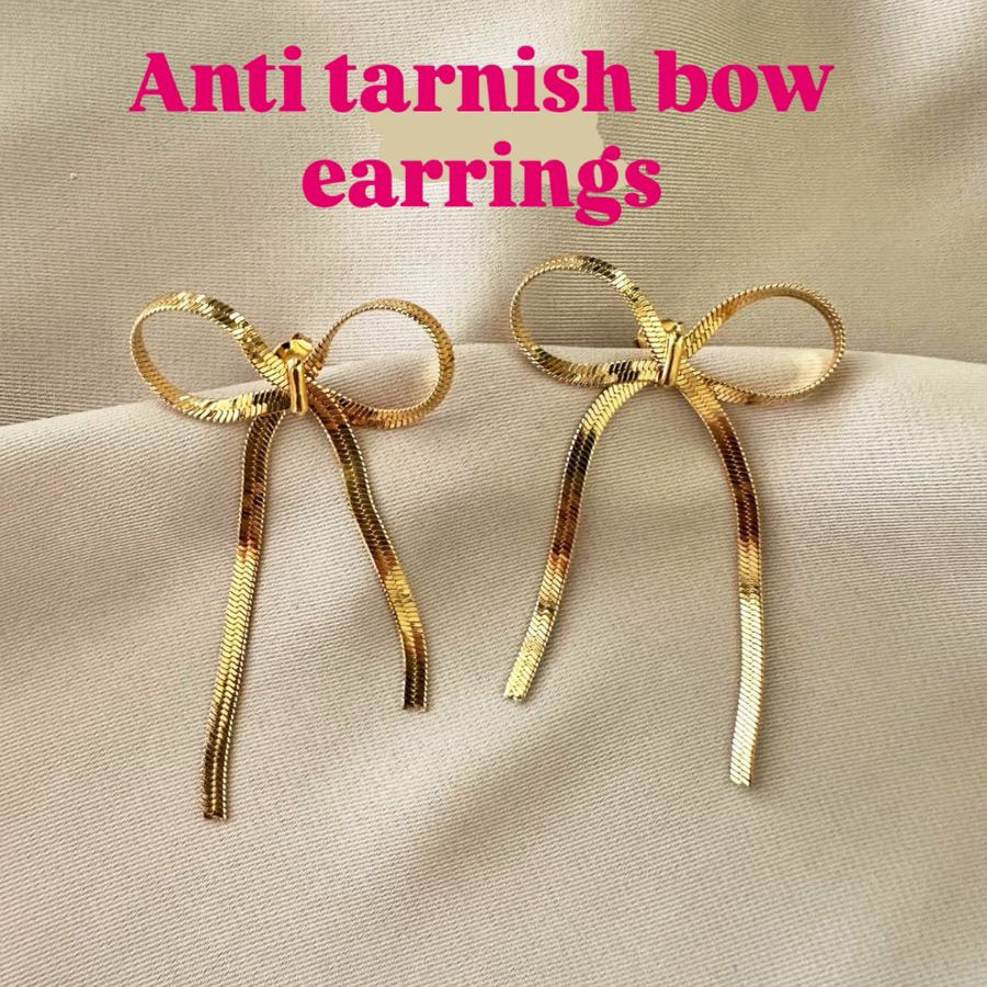 Gold bow-shaped earrings on a black glove